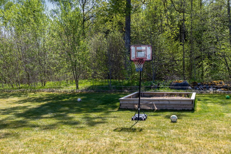 Sandlåda och basketkorg omgivna av grönska