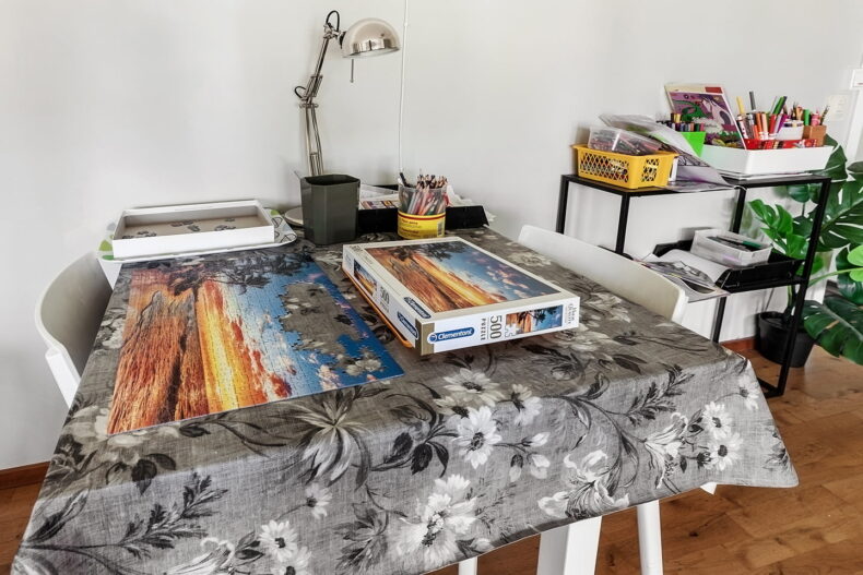 Litet bord med ett pågående pussel på, intill är en liten hylla med pennor och pyssel