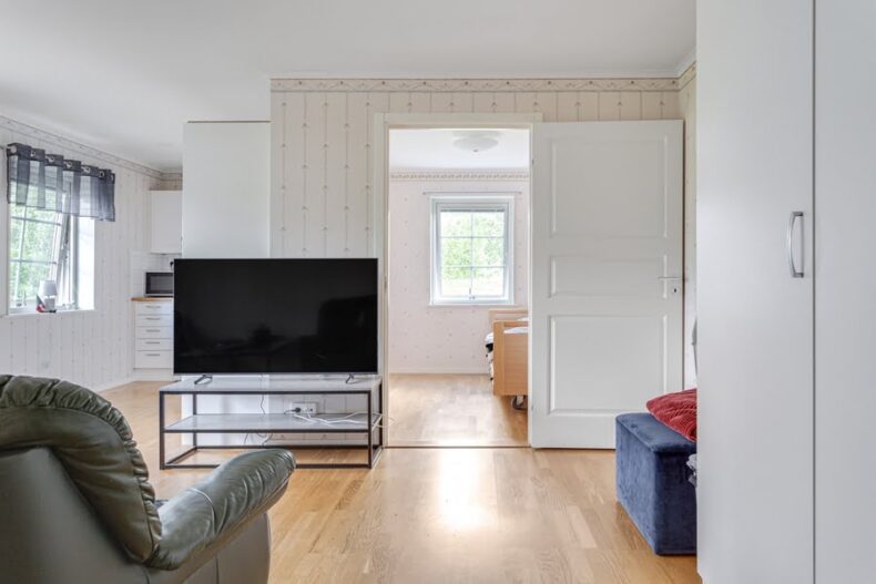 En av boendets lägenheter med fåtölj, TV, kök och en öppen dörr in till sovrummet