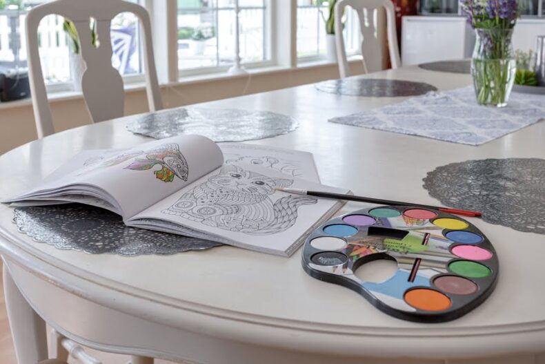 Närbild på en öppen målarbok med ett kattmotiv, bredvid en palett med vattenfärger och en pensel.