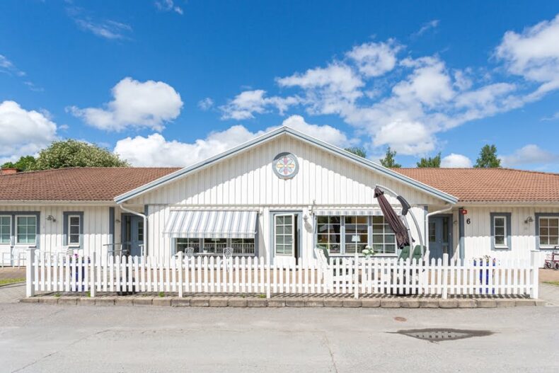 Boendet sett från uppfarten, med ett lågt vitt staket framför.