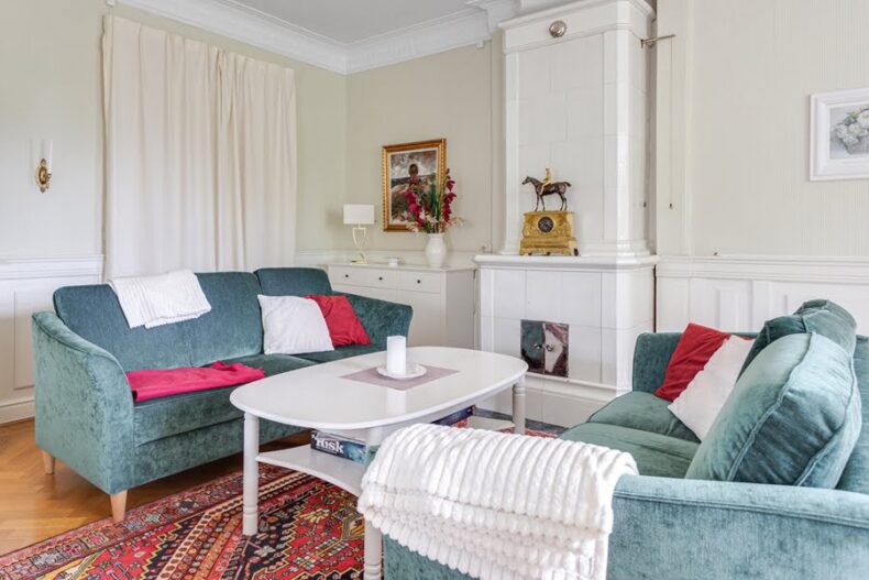 Två sammets-soffor och ett soffbord vid en kakelugn