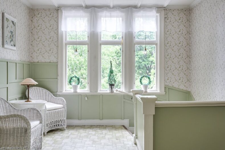 En lugn hörna ovanför en trappa, med två korgstolar framför smala ljusa fönster