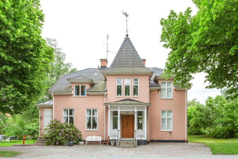 Rosa Villan sedd framifrån med grusplan framför och träd omkring