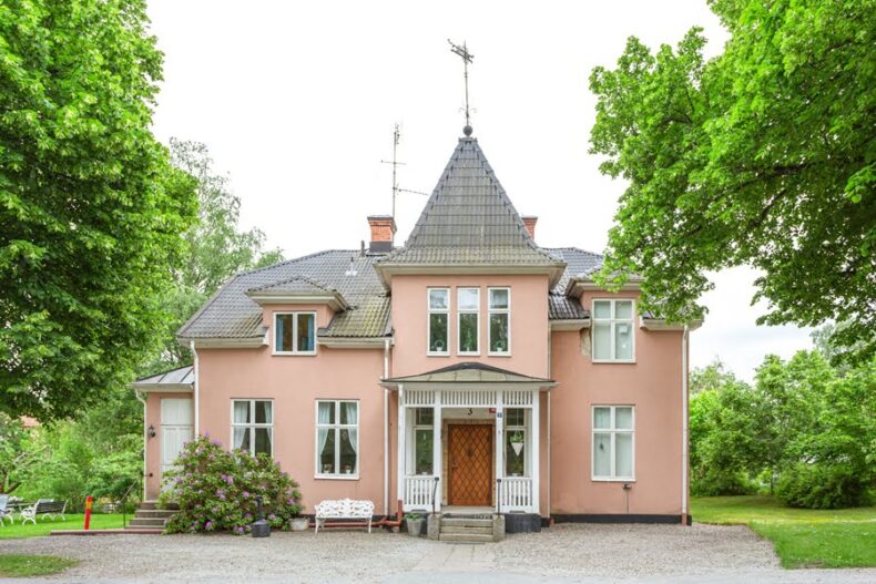 Rosa Villan sedd framifrån med grusplan framför och träd omkring