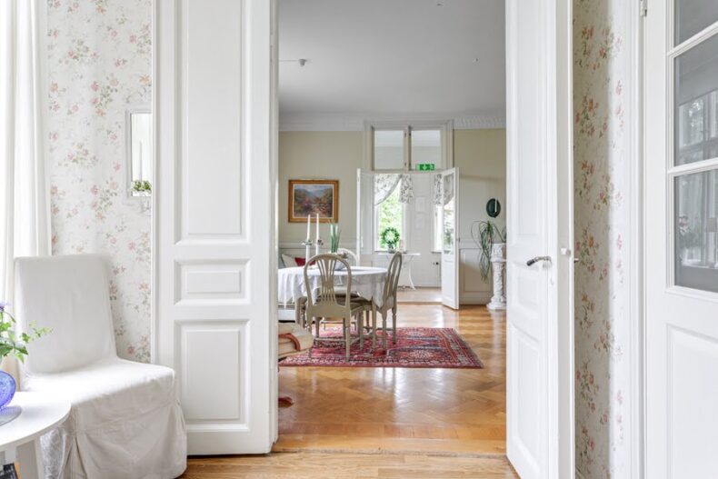 Ett dörrhål in till en matsal med parkettgolv, persisk matta och gammaldags möbler