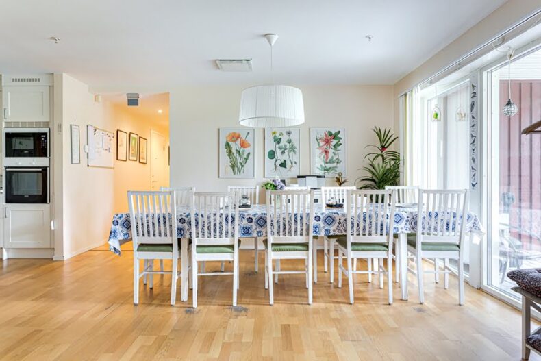 Ett långbord med blommig duk i ett ljust rum med flera blomstermålningar på väggarna