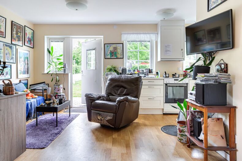 En av boendets lägenheter med kokvrå, fåtölj, soffa, krukväxter samt mycket konst på väggarna,