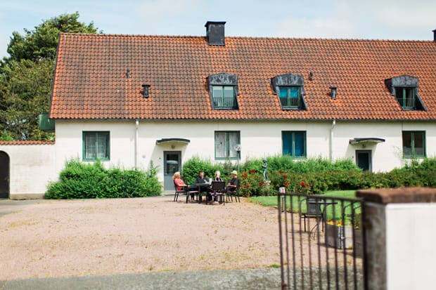 Fyra personer sitter och fikar på grusplanen framför en av verksamhetens byggnader